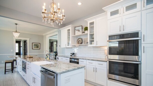 A modern kitchen with white cabinetry, a large island, stainless steel appliances, and a chandelier.