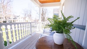 A wooden deck with a white railing, a round wooden table, and a white pot with a green plant.