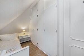 Une chambre à coucher avec un lit, une table de chevet, une lampe et une armoire blanche.