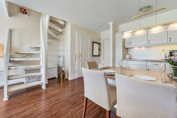 A modern kitchen with white cabinets, a wooden dining table, and a staircase leading to an upper floor.