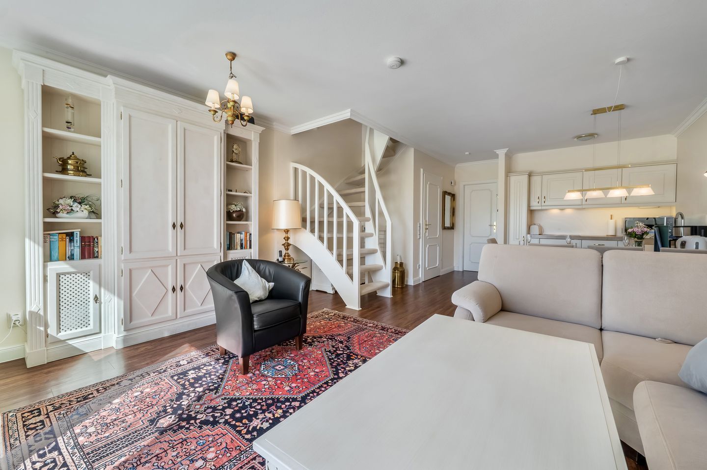 A spacious living room with a staircase, a black leather armchair, a white sofa, and a patterned rug.