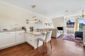 Una cocina moderna con muebles blancos, un comedor con mesa y sillas, y una sala de estar con sofá y televisor.