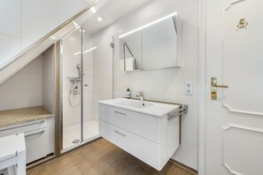 A modern bathroom with a glass shower enclosure, a white vanity with a mirror, and a wooden floor.