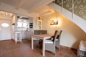 Ein Essbereich mit Holztisch und Korbstühlen, im Hintergrund eine Küche und eine Treppe mit Wandverzierungen.