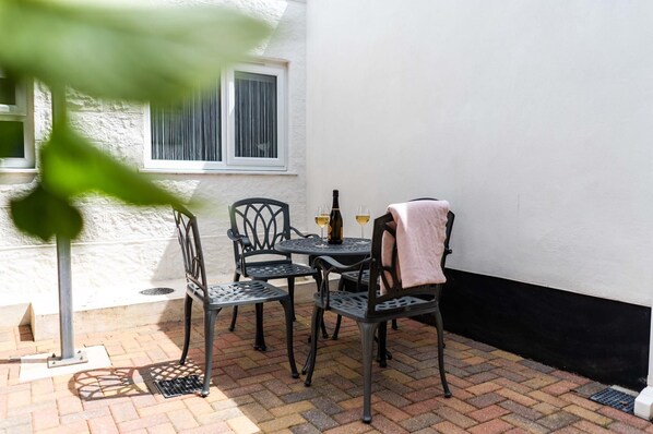 An outdoor patio with a table and four chairs, a bottle of wine, and two glasses on the table.