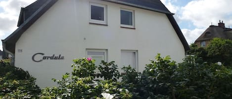 Una casa blanca con el nombre 'Cordula' en la fachada, rodeada de vegetación y flores.