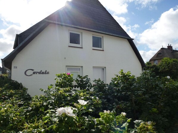 Une maison blanche, portant le nom « Cordula » sur sa façade, entourée de verdure et de fleurs.