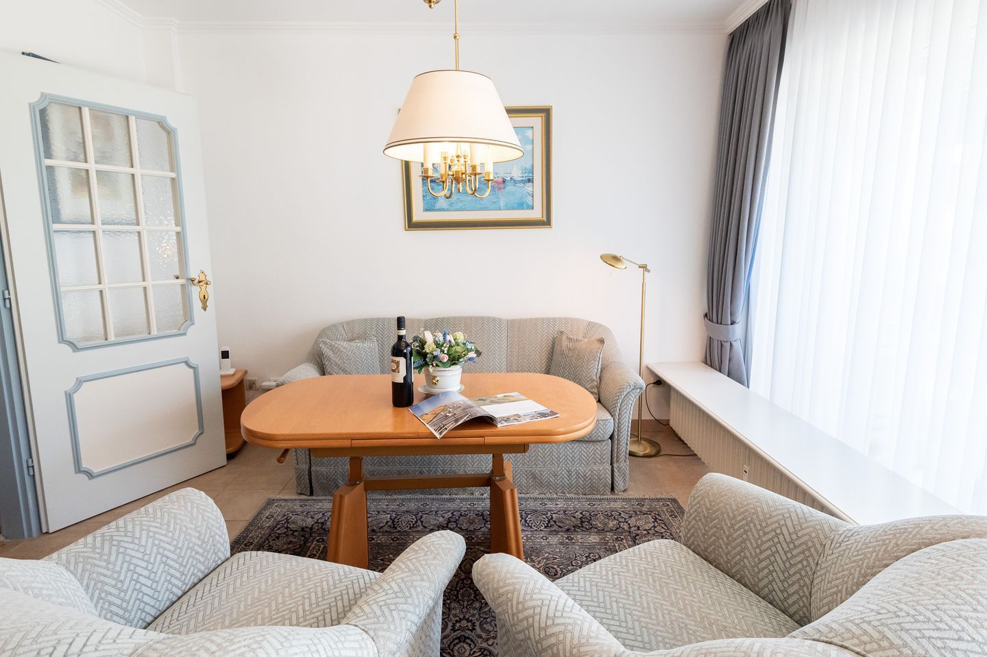 Une pièce chaleureuse avec une table en bois, deux fauteuils, un canapé, une lampe sur pied et un tableau au mur.