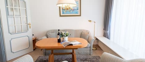 Una habitación acogedora con una mesa de madera, dos sillones, un sofá, una lámpara de pie y un cuadro en la pared.