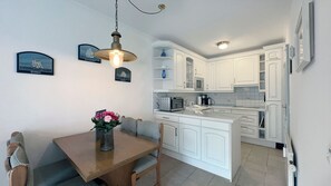 Ett kompakt kök med vita skåp, en köksö och en matplats med ett träbord och stolar.