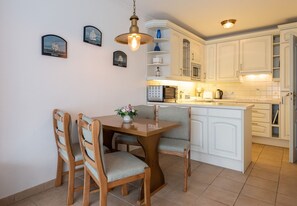 A dining area with a wooden table and chairs, a vase of flowers, and a kitchen with white cabinets and a microwave.