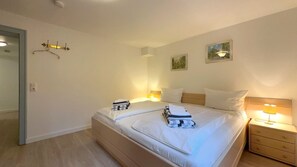 A neatly made double bed with white linens, two bedside tables with lamps, and a wall-mounted coat rack.