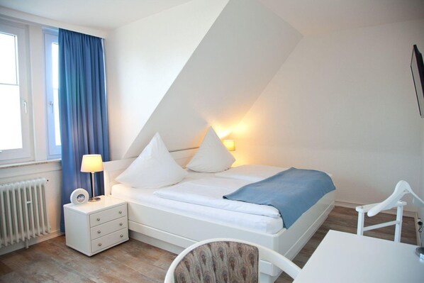 Een slaapkamer met een bed, nachtkastje, lamp en een stoel.