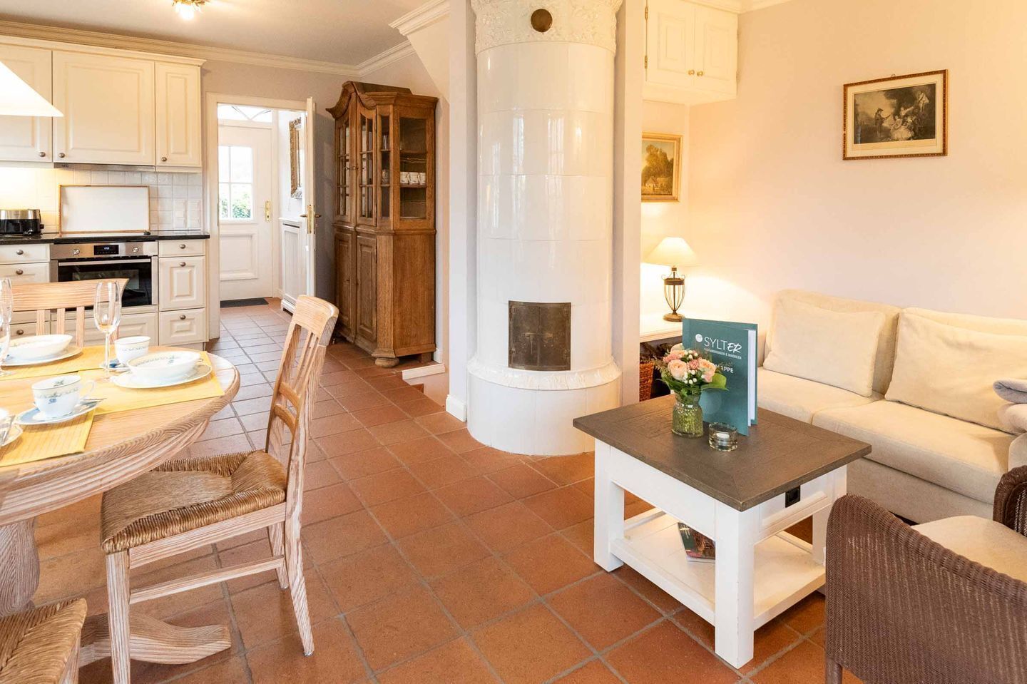 A cozy living room with a white sofa, a dining area with a round table and chairs, a fireplace, and a kitchen with white cabinets and a stove.