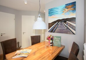 Uma área de refeições com mesa de madeira, cadeiras, luminária pendente branca, pintura de uma ponte e um folheto sobre a mesa.