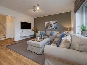 A modern living room with a flat-screen TV, a sectional sofa, a coffee table, and a staircase leading to another level. - Dacklünen - Dieses Ferienhaus in Beliebter Wohngegend von Wenningstedt Bietet Maximal 6 Personen auf (Wenningstedt-Braderup (Sylt))