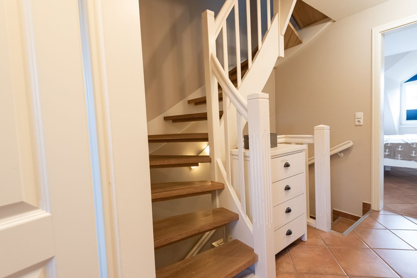 A staircase with wooden steps and white railings, leading to a bedroom with a bed and a view of the outside.