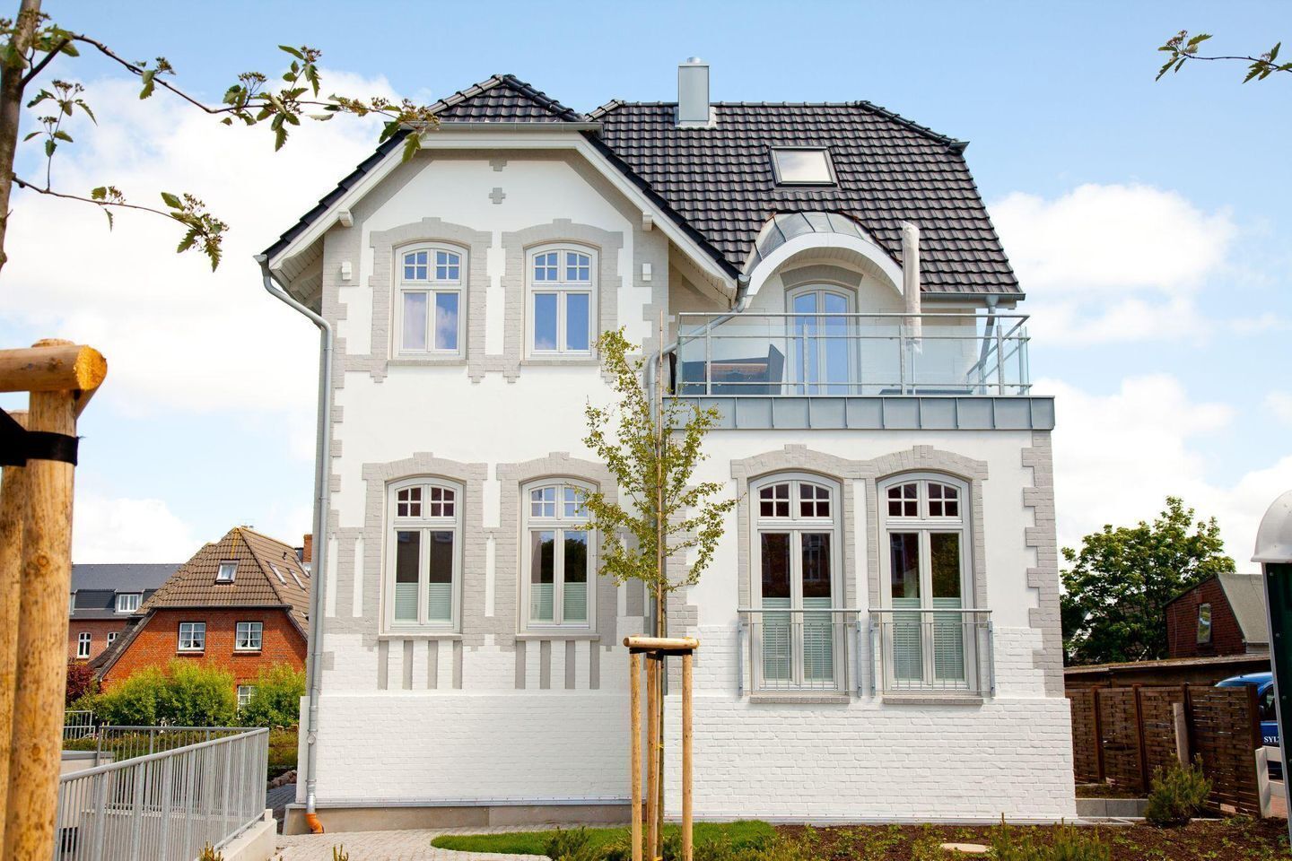 A two-story house with a white facade, multiple windows, and a balcony.