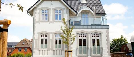 A two-story house with a white facade, multiple windows, and a balcony.