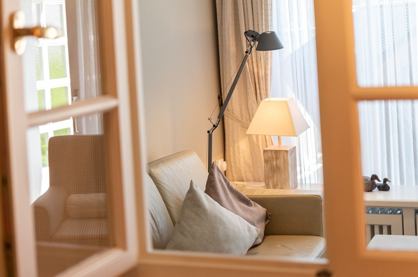 Une pièce confortable avec un canapé, deux lampes et une vue sur l’extérieur à travers une fenêtre ornée de rideaux.