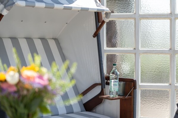 A cozy room with a striped sofa, a small table with a bottle, and a window with a view. - C-haus Christine, App.20 - Ferienwohnung in Direkter Strandnähe mit ca. 65 m² Wohnfläche und 3 (Wenningstedt-Braderup (Sylt))
