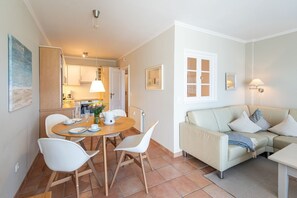 Uma sala de estar moderna com um sofá bege, uma mesa de jantar com cadeiras e uma cozinha ao fundo.