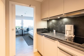 Cocina moderna con encimera negra, cafetera y vistas a un comedor con mesa y sillas.