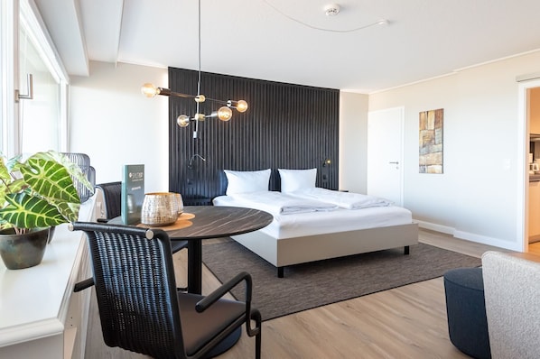 Un dormitorio moderno con cama, mesita de noche, silla y un rincón comedor con mesa y sillas.