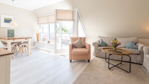 Ein modernes Wohnzimmer mit Sofa, Sessel, Couchtisch und einem Essbereich mit Stühlen und Tisch.