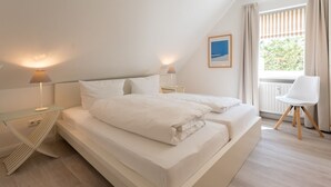 Ein modernes Schlafzimmer mit einem großen Bett, Nachttischlampen, einem gerahmten Bild und Blick auf Grün.