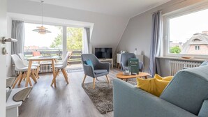 Ein modernes Wohnzimmer mit Essbereich, großen Fenstern und einem Fernseher.