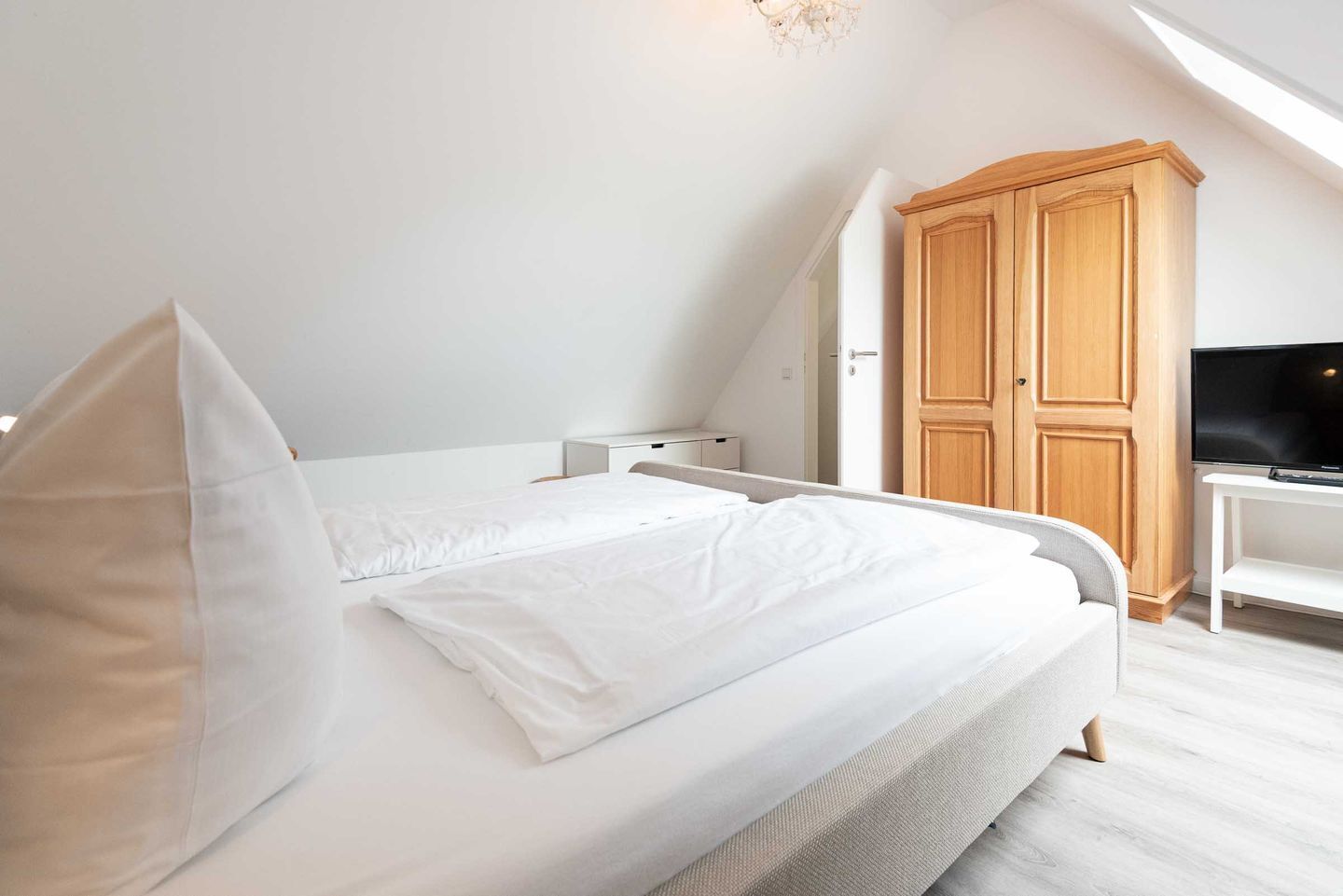 Une chambre à coucher avec un lit, une armoire en bois, un bureau avec une télévision et un lustre.