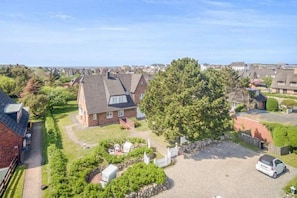 A residential area with houses, a large tree, and a gravel driveway. - Sylterpferdchen, Landhaus Köövenhüs - Gemütliche Ferienwohnung mit 3 Zimmern auf ca. 73 m², für max (Wenningstedt-Braderup (Sylt))
