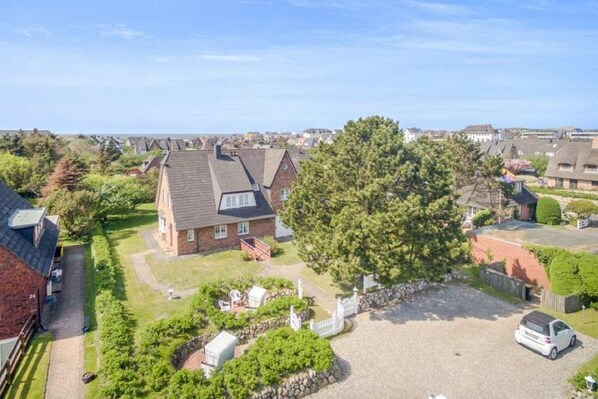 A residential area with houses, a large tree, and a gravel driveway. - Sylterpferdchen, Landhaus Köövenhüs - Gemütliche Ferienwohnung mit 3 Zimmern auf ca. 73 m², für max (Wenningstedt-Braderup (Sylt))