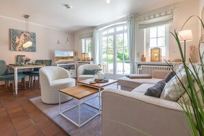 A well-lit living room with a dining area, large windows, and a view of the outdoors. - Sylterpferdchen, Landhaus Köövenhüs - Gemütliche Ferienwohnung mit 3 Zimmern auf ca. 73 m², für max (Wenningstedt-Braderup (Sylt))