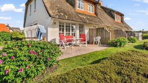 Una casa con tetto di paglia, un patio con mobili da esterno e un giardino curato.