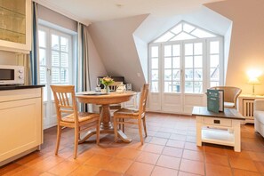Una cocina acogedora con una mesa de comedor, sillas y un microondas. Hay una ventana con cortinas, una puerta y vistas a edificios.