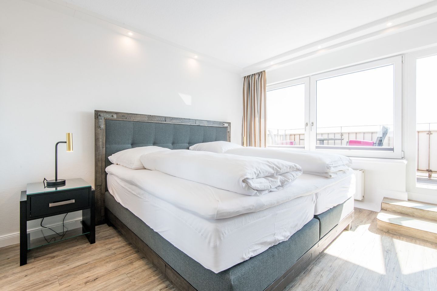 Una habitación de hotel moderna con una cama grande, una mesita de noche y un ventanal con cortinas.