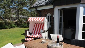 A patio with a wooden table, a striped lounge chair, and a bottle of wine.