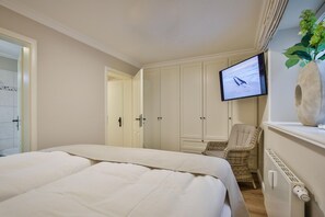 A bedroom with a bed, a television, a chair, and a plant. - Zita App. 2 - Moderne 3-zimmer Ferienwohnung auf ca. 84 m² Wohnfläche, für bis zu 4 Personen (Wenningstedt-Braderup (Sylt))