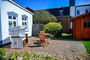 Une maison blanche avec un patio dallé, des meubles en osier et une clôture en bois.
