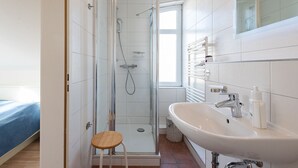 Un baño moderno con cabina de ducha de vidrio, un lavabo blanco y un taburete de madera.