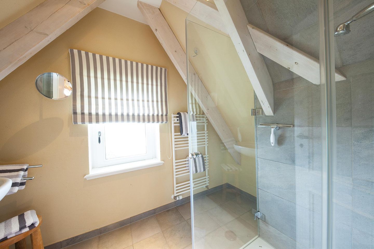 A bathroom with a shower, a window with striped blinds, a towel rack, and a mirror.