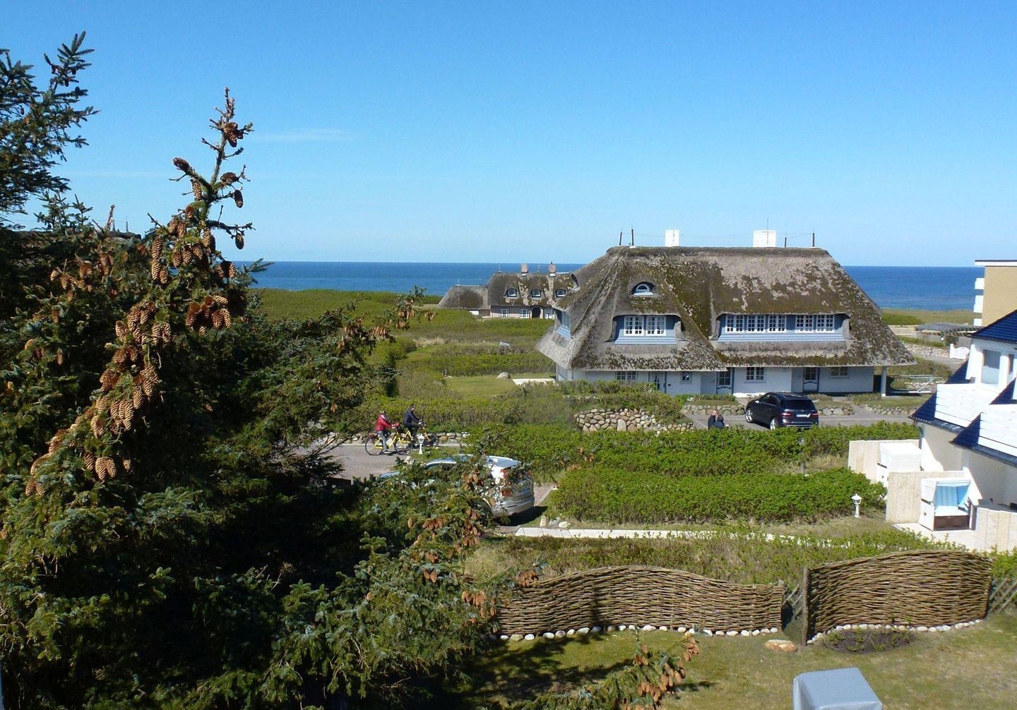 Ein Haus mit einem Strohdach, einem Garten und Blick aufs Meer.