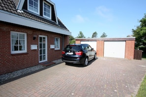 A two-story brick house with a car parked in the driveway and a garage attached to the right.