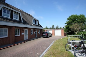 A two-story brick building with a car parked in the driveway and a bicycle rack on the right.