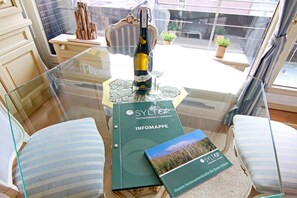 Une pièce avec une table en verre, deux chaises à rayures, une bouteille de vin et une brochure intitulée « SYLTER FERIENWOHNUNGEN & IMMOBILIEN INFOMAPPE ».
