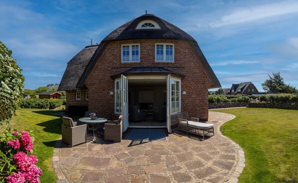 A brick house with a thatched roof, a stone patio, and outdoor seating. - The thatched beach house - Fantastic thatched beach house with 6 rooms on approx. 200 m², (Wenningstedt-Braderup (Sylt))