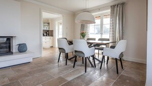 Zona pranzo con tavolo e sedie, lampadario e vista all'esterno tramite una finestra con tende.