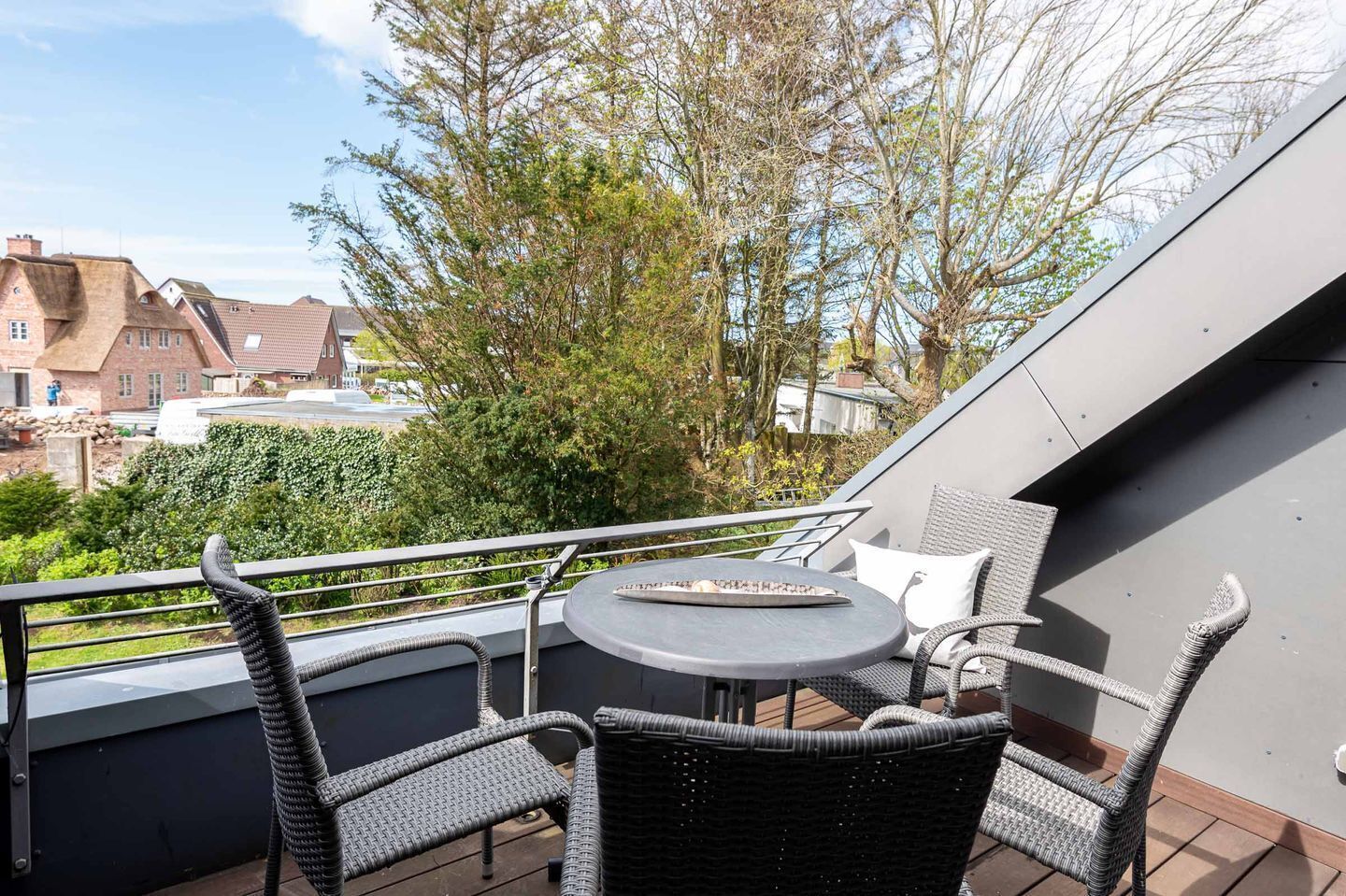 A balcony with wicker furniture, a round table, and a view of buildings and trees.